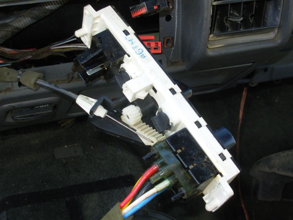 Removed steering column ignition and switch assembly with white housing and wires under a dash
