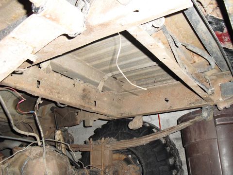 1986 Ford Bronco - Undercarriage view shows rusty frame, leaf springs, and tire of a truck.