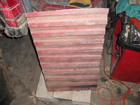 1986 Ford Bronco - A red corrugated metal panel is shown, with a portion of a red vehicle's tail light visible on the left side.