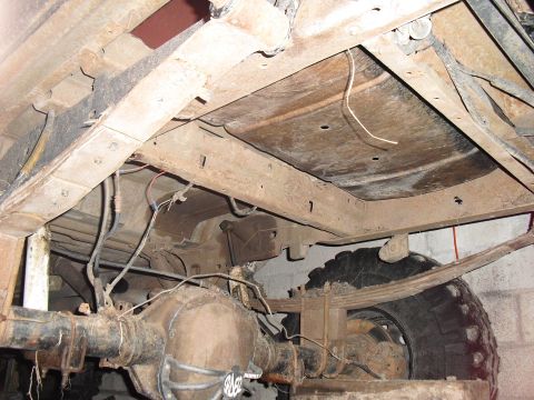 1986 Ford Bronco - The rusty undercarriage of a vehicle, revealing its rear axle and suspension components.