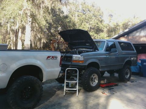 1995 Ford Bronco - Two trucks are parked outside a garage, one with its hood up for maintenance.