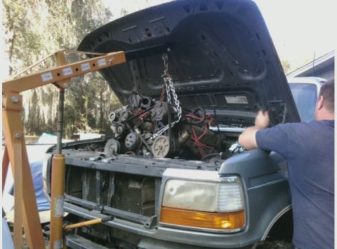1995 Ford Bronco - A person uses an engine hoist to remove the engine from a truck with its hood open.