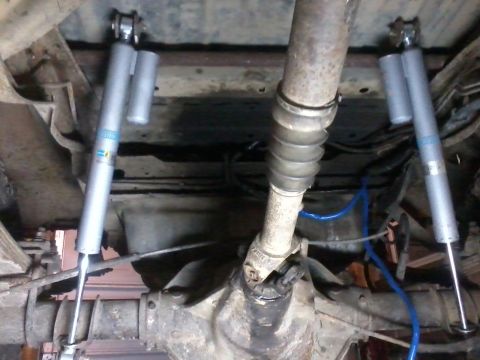 1995 Ford Bronco - Close-up view of rear shock hoops and Bilstein shocks, with a driveshaft visible.