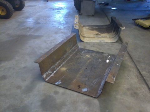 1995 Ford Bronco - A fabricated metal skid plate sits on a concrete floor next to another part.