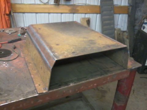 1995 Ford Bronco - A rusty metal skid plate sits on a workbench in a garage.