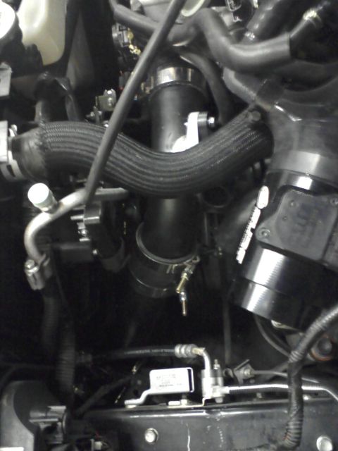 1987 Ford Bronco - Detail shot of engine components, including various hoses and a silver sensor with readable text.