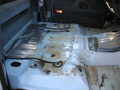 1994 Ford Bronco - The interior floor of a vehicle is shown with exposed metal and wiring, indicating it is stripped down.