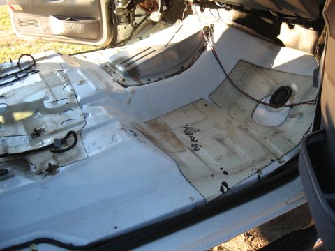1994 Ford Bronco - The bare metal interior floor of a vehicle is visible, with wiring and mounting points exposed after carpet removal.