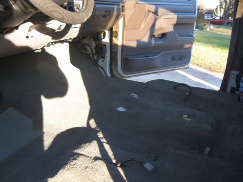 1994 Ford Bronco - The interior carpet and door panel of a vehicle are visible, with exposed wiring and a shadow cast across the floor.