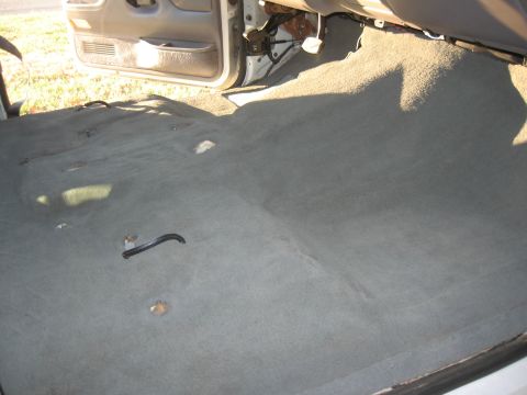 1994 Ford Bronco - The interior carpet of a vehicle has been removed, revealing the floor and parts of the dashboard and door.