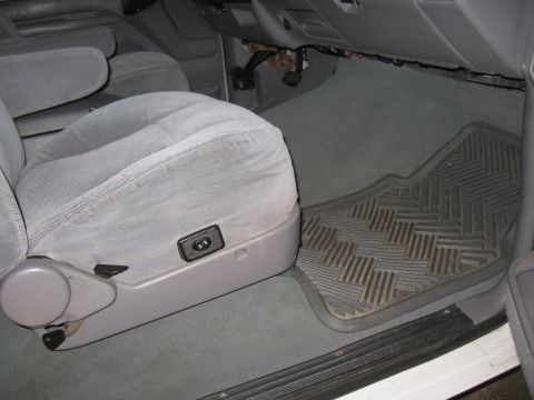 1994 Ford Bronco - The interior of a vehicle shows gray carpet and a black rubber floor mat in front of a fabric seat.