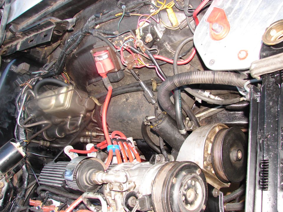 Engine bay with lots of wires, hoses, a brake fluid reservoir, and an AC compressor