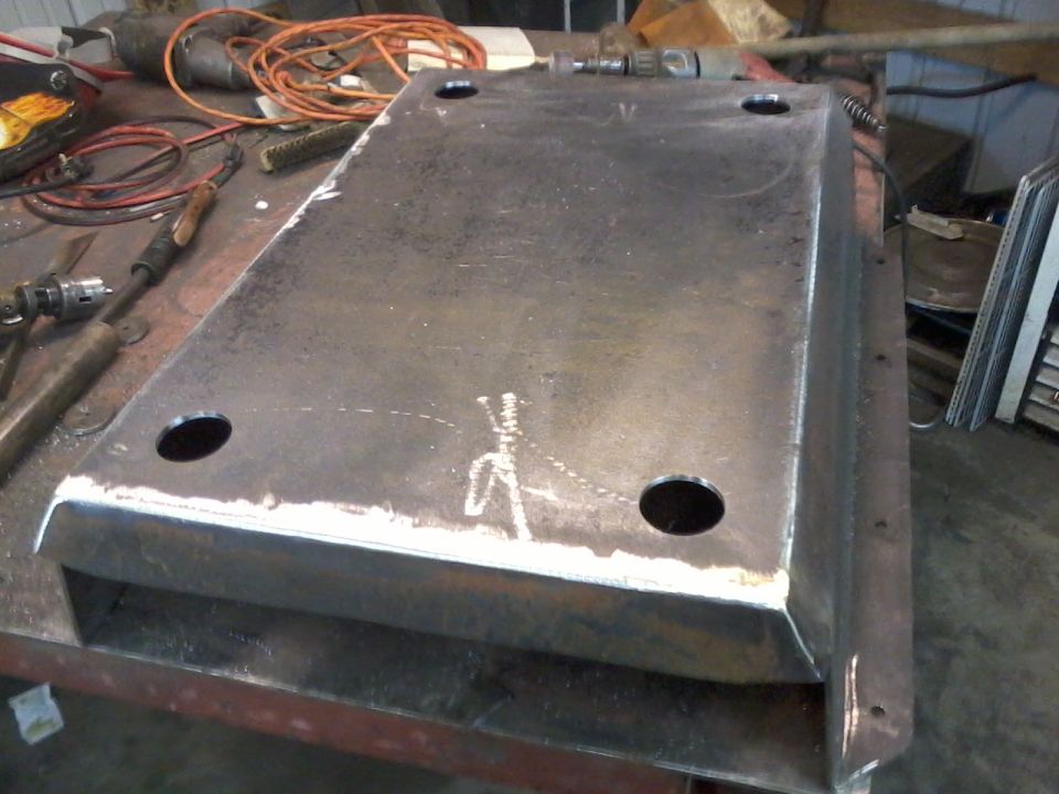 Metal skid plate with four bolt holes, sitting on a workbench with tools