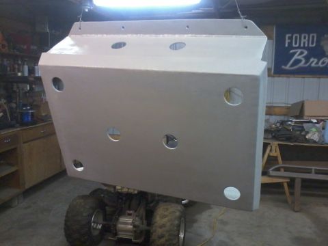 1995 Ford Bronco - A large skid plate is suspended in a garage, with an ATV visible beneath it and a Ford Bronco banner on the wall.