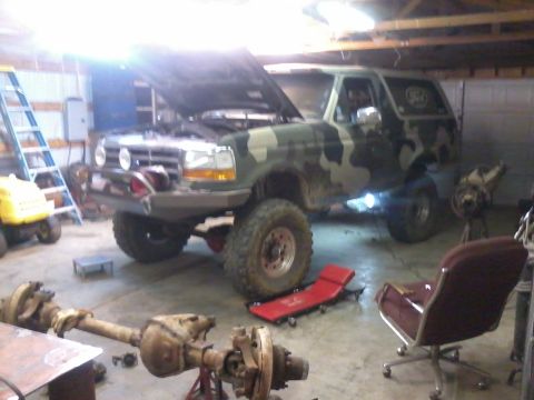 1995 Ford Bronco - 1995 Ford Bronco undergoing maintenance in a garage with its hood up and front axle removed.