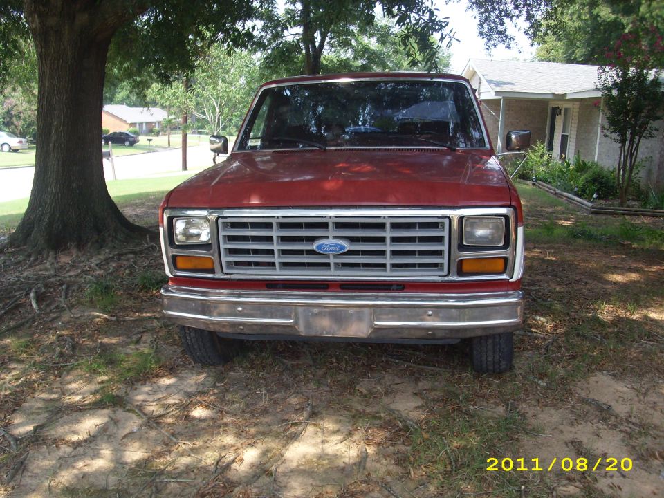Red 1987 Ford F-150 front view, parked under a tree