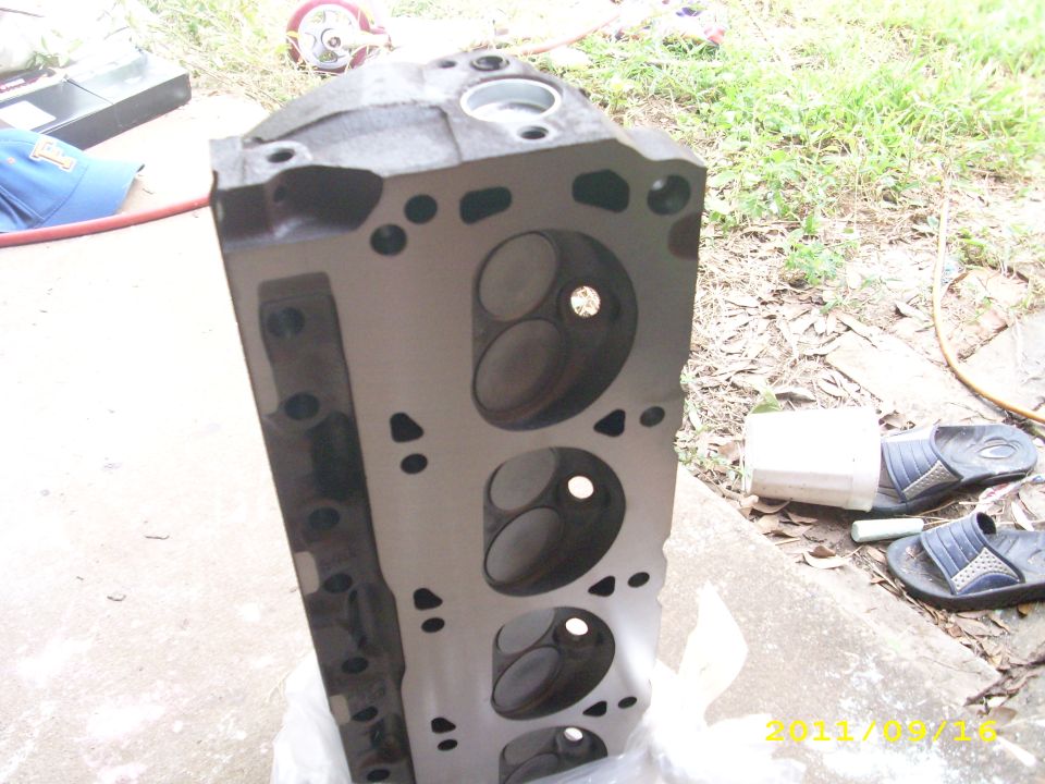 Engine cylinder head with visible valves and ports, resting on a white plastic bag outdoors
