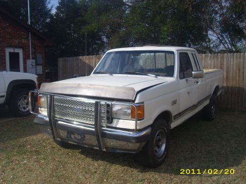 1990 Ford F-150 - A white 1990 Ford F-150 pickup truck is parked in a grassy area next to a brick building.
