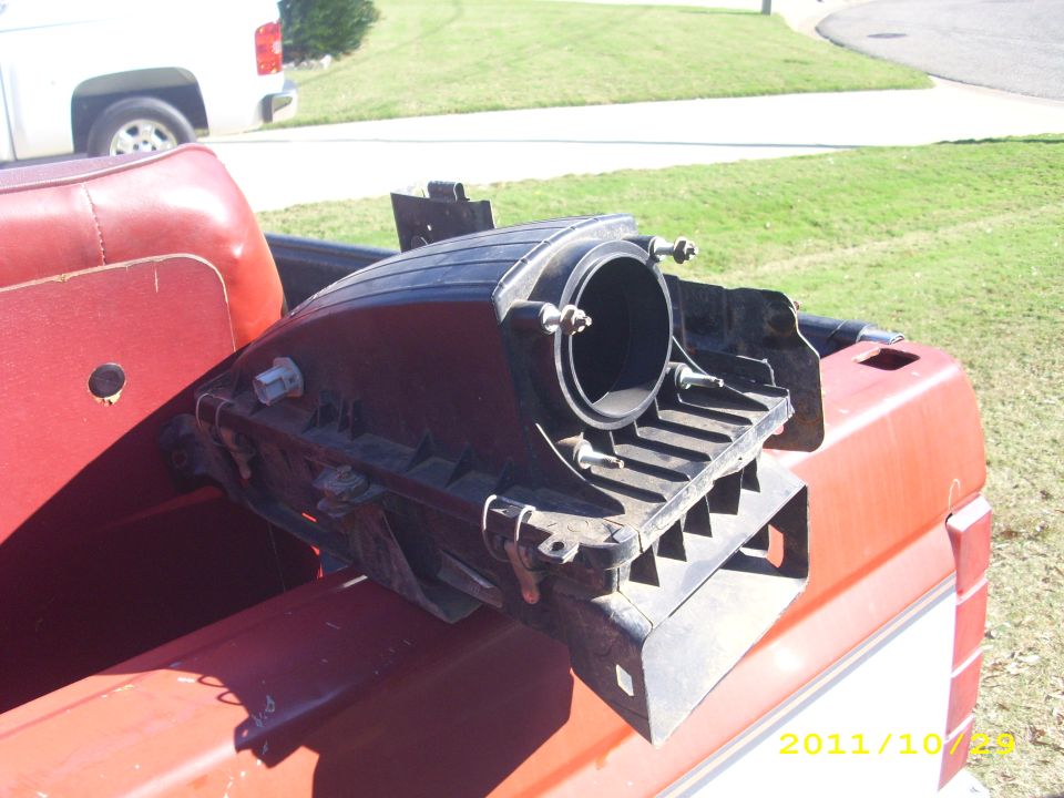 Black air intake part in red truck bed, white truck in background