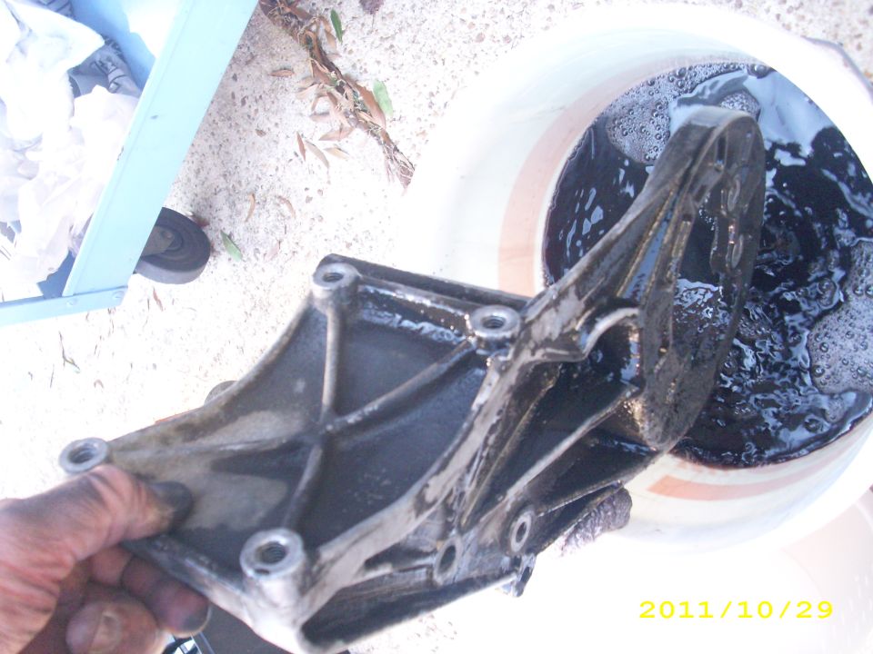 Dirty metal engine bracket being soaked in a bucket of dark liquid