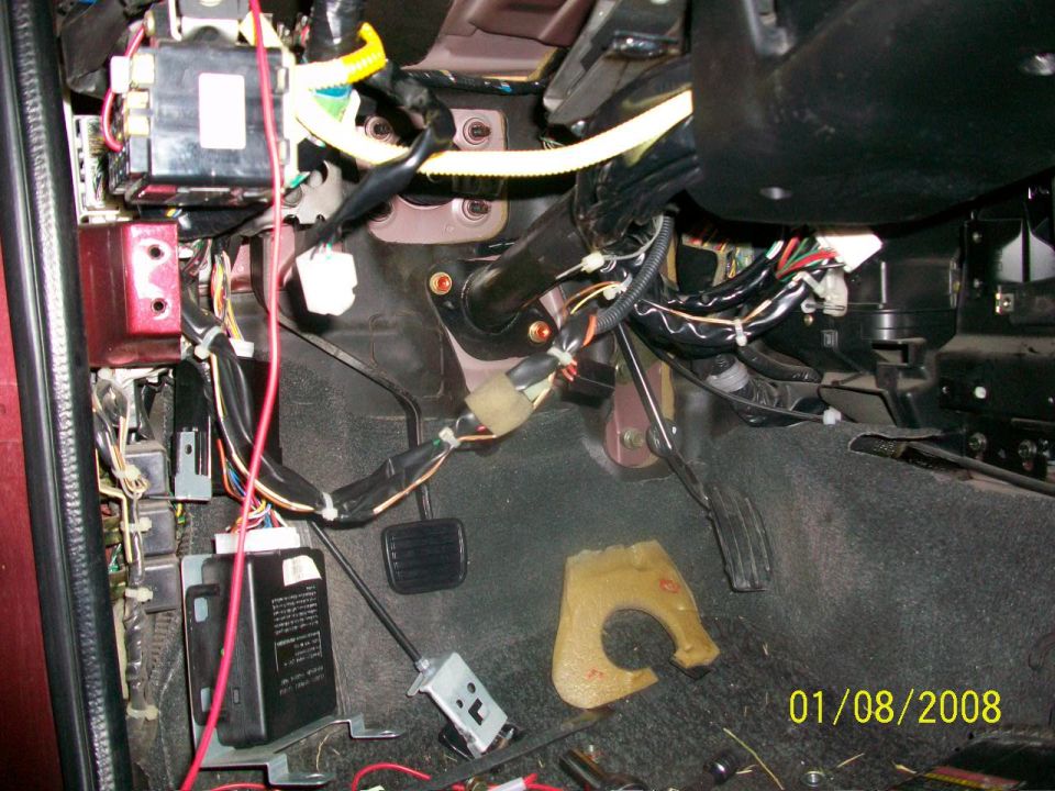 Vehicle interior showing exposed wiring, pedals, and fuse box