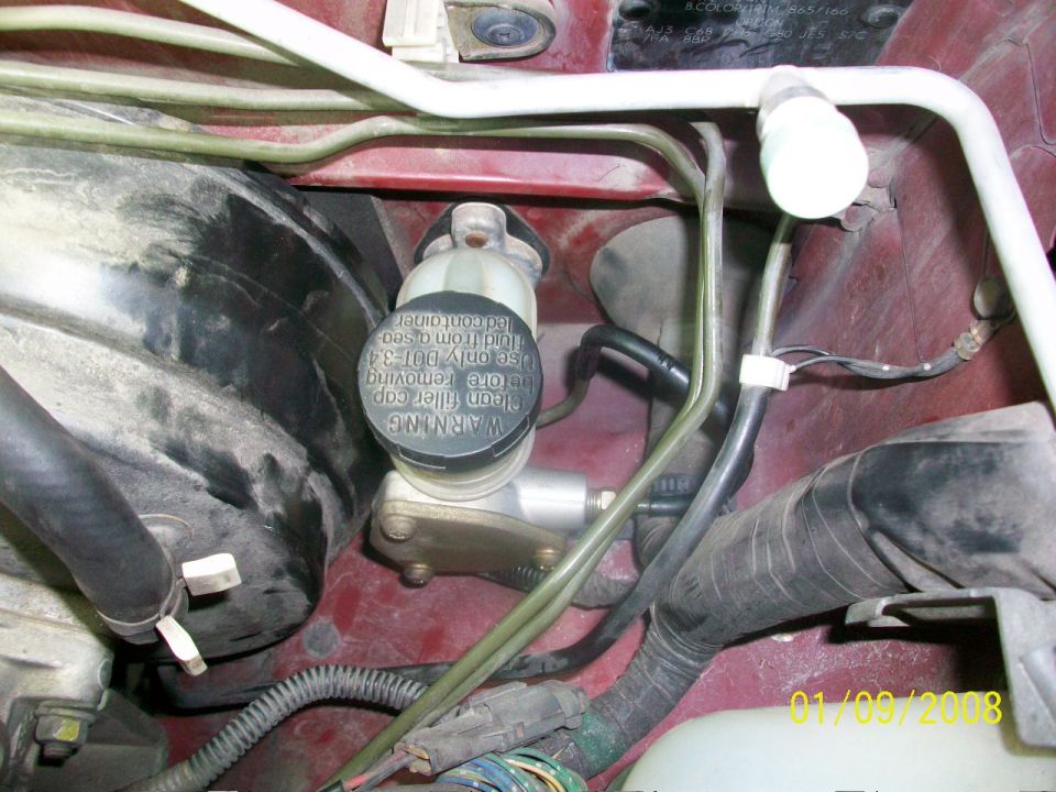 Engine bay with brake fluid reservoir, hoses, and wiring. Red painted metal body