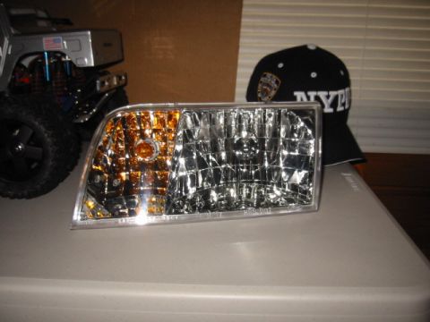 1998 Ford Crown Victoria - A headlight assembly, likely for a 1998 Ford Crown Victoria, sits on a surface with other items.