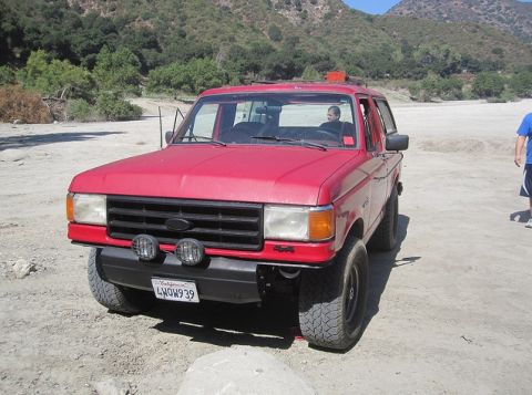 1988 Ford Bronco - This red 1988 Ford Bronco is shown in a dry, outdoor setting with a person inside and another person standing nearby.