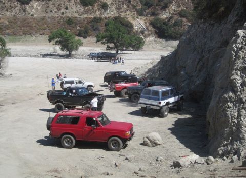 1988 Ford Bronco - Multiple Ford Broncos and other SUVs gathered in a dirt area, possibly for off-roading.
