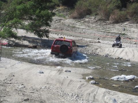 1988 Ford Bronco - A red 1988 Ford Bronco navigates a water crossing, with an ATV visible on the bank.