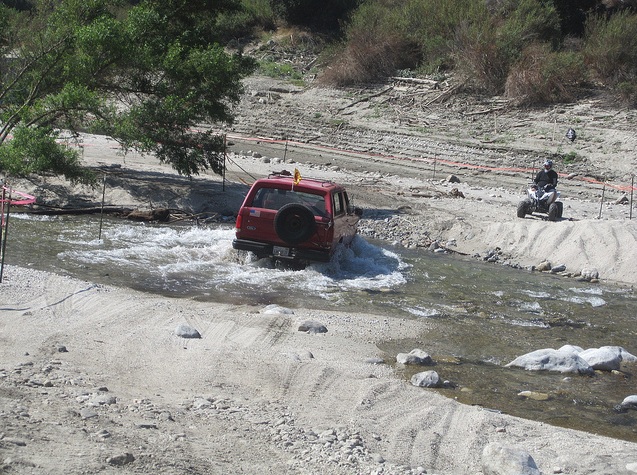 Red 1988 Ford Bronco driving through a shallow river, rear view