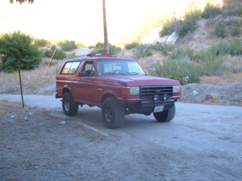 1988 Ford Bronco - This red Ford Bronco is parked on a dirt road with hills in the background.