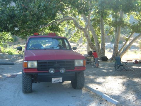 1988 Ford Bronco - Red 1988 Ford Bronco parked under large trees at a campsite.