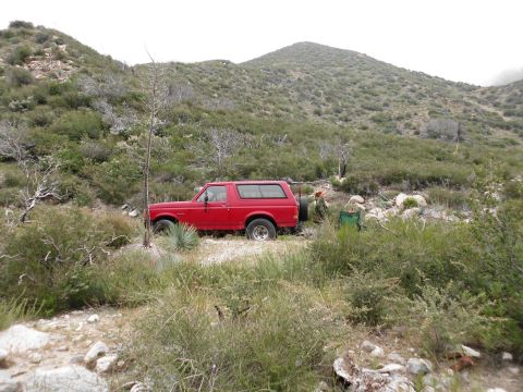 1988 Ford Bronco - A red 1988 Ford Bronco is parked on a dirt road in a dry, hilly landscape, surrounded by brush and rocks.