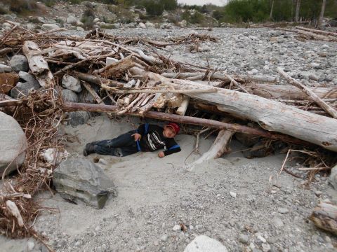 1988 Ford Bronco - A person rests in a makeshift shelter formed by driftwood and rocks in a dry riverbed.