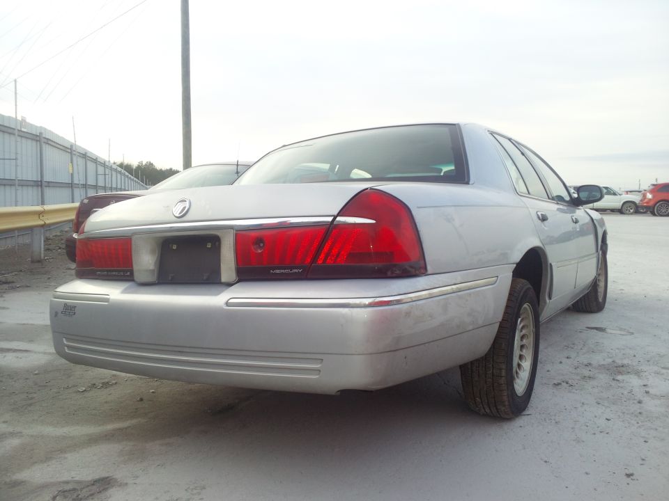 Silver Mercury Grand Marquis sedan, rear three-quarter passenger-side view, parked on gravel lot