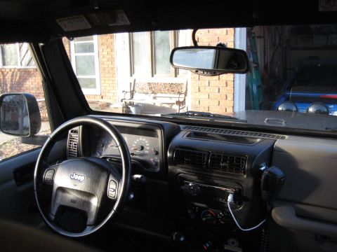 2005 Jeep Wrangler - Interior view of a 2005 Jeep Wrangler, showing the dashboard, steering wheel, and rearview mirror. The vehicle appears to be parked outside…