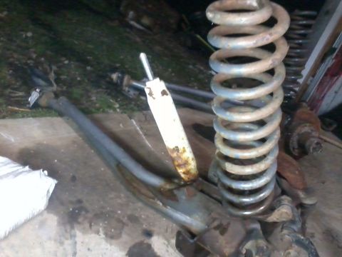 1995 Ford Bronco - Close-up of vehicle suspension parts, including a coil spring and shock absorber, with visible rust.