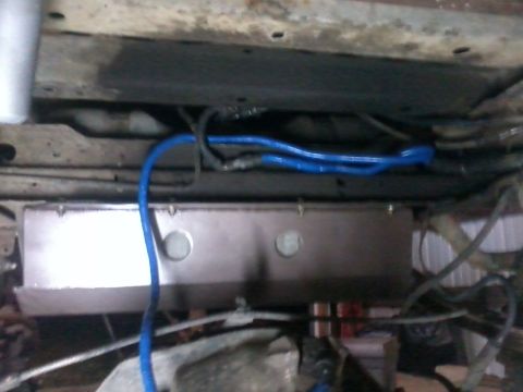 1995 Ford Bronco - Underside view of a metal gas tank skid plate with blue fuel lines.