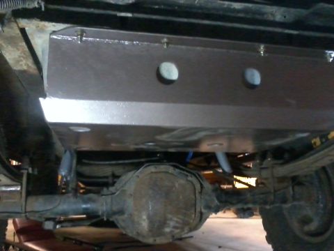 1995 Ford Bronco - Underside view of a vehicle's rear axle and suspension, with a brown skid plate installed over the gas tank.
