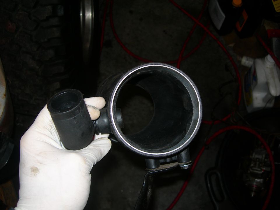 Gloved hand holding black intake tube with attached hose