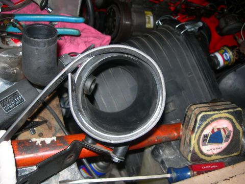 1984 Ford Bronco - A close-up view of automotive parts, including a large rubber hose and an air filter housing, in a workshop setting.