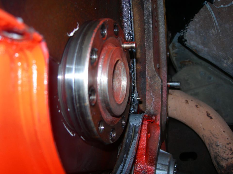 Close-up of a metal flange with bolt holes, attached to red-painted components and a dark metal bracket
