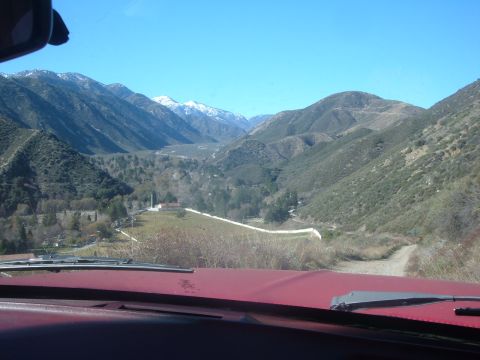 1988 Ford Bronco - View from inside a red vehicle driving on a dirt road through a scenic mountain valley.