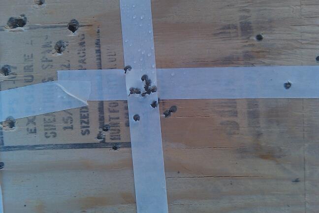 Wooden surface with tape and bullet holes. Text visible on surface