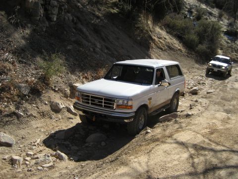 1996 Ford Bronco - Two SUVs navigate a challenging off-road trail on a sunny day.