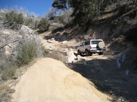 1996 Ford Bronco - A white 1992 Ford Bronco navigates a challenging off-road path with rocky terrain and sparse vegetation.