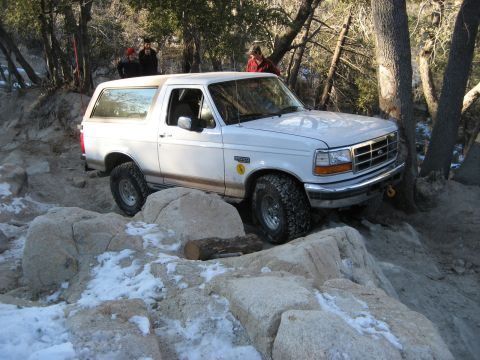 1996 Ford Bronco - A white 1996 Ford Bronco is shown traversing a challenging rocky terrain with patches of snow.