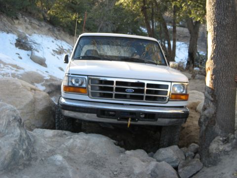 1996 Ford Bronco - A white Ford Bronco is shown off-roading on a rocky trail with patches of snow.