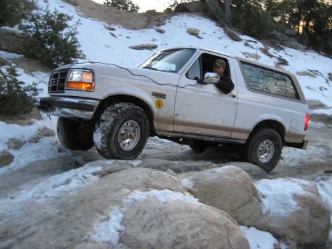 1996 Ford Bronco - White 1996 Ford Bronco tackling a challenging off-road trail with snow and rocks.
